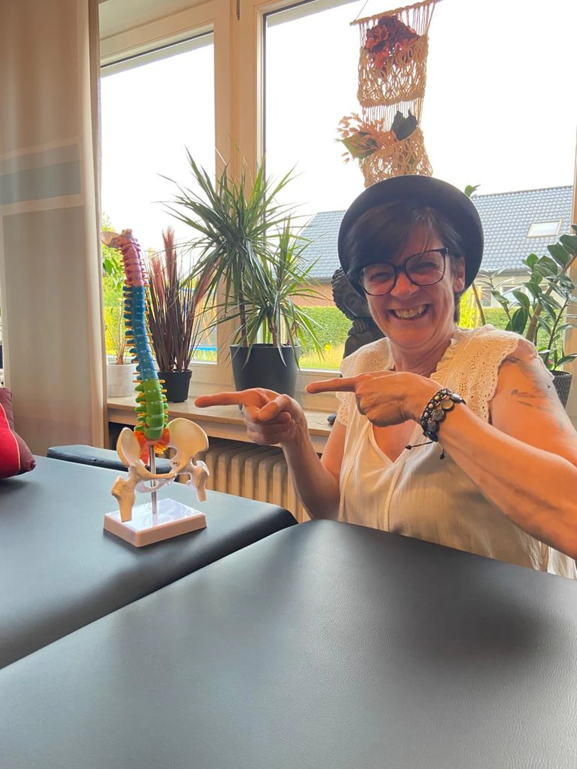 Manuela Möller sitzt auf einem Stuhl und zeigt auf ein menschliches Wirbelsäulenmodell